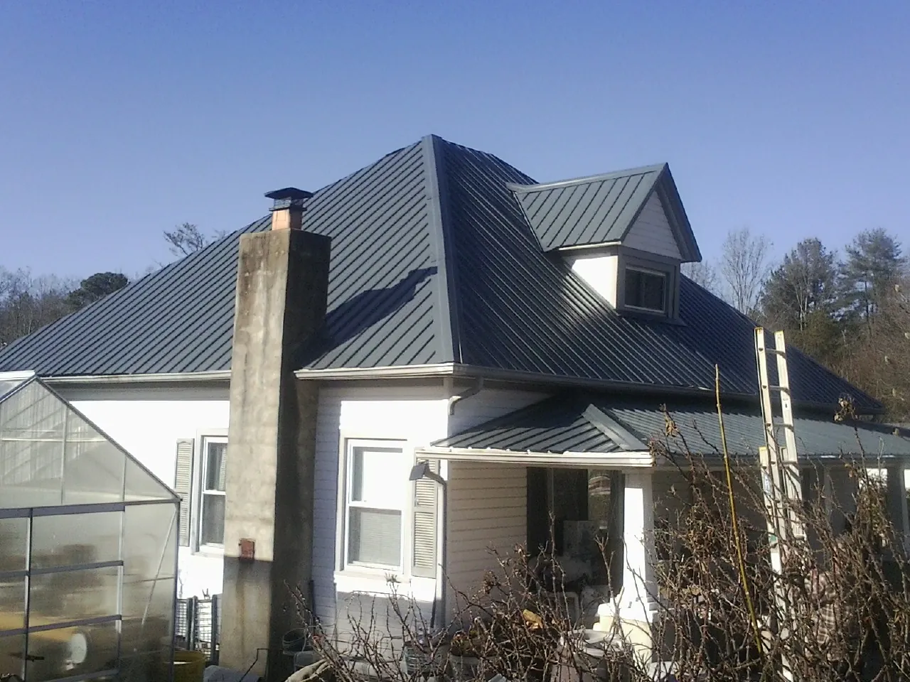 Dark blue standing seam metal roof on a white farmhouse with dormer — Slate & Tile Roof Repair by Roofing Brothers in Peralta