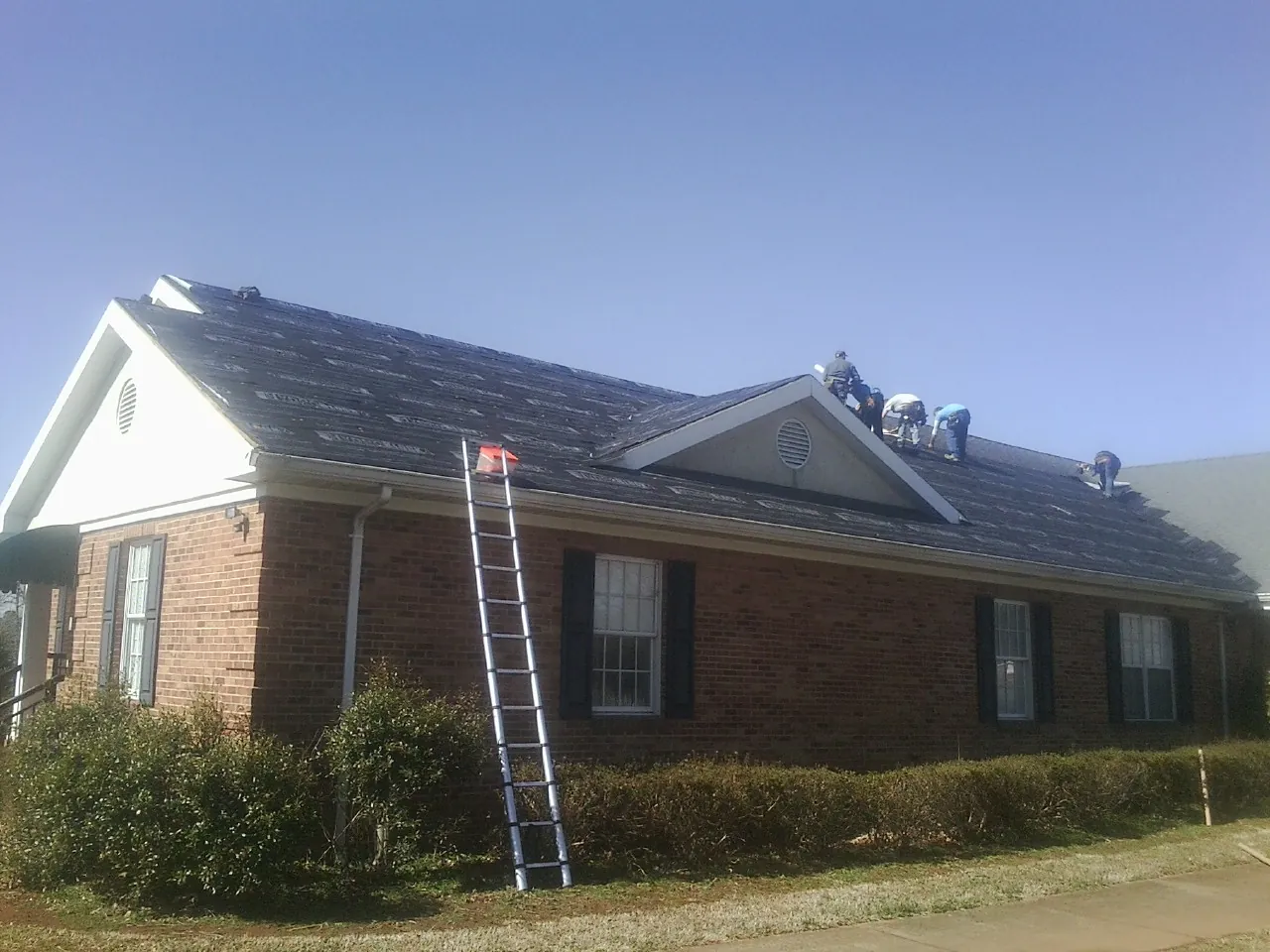 Crew tearing shingles off a brick ranch roof with a ladder set — Emergency Roof Repair work by our crew in Peralta