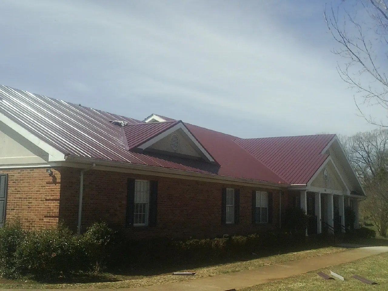 Red metal roof with gabled entries on a long brick building, from a Hail Damage Roof Repair job in Peralta