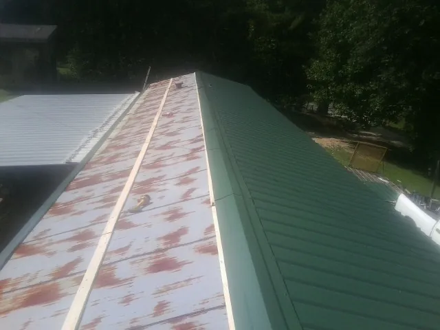 Old rusted panels beside newly installed green metal roofing — Wind Damage Roof Repair by Roofing Brothers in Peralta