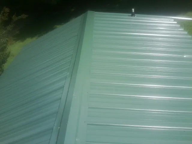 New green metal panels meeting at the ridge of a roof — Flat Roof Repair work by our crew in Peralta