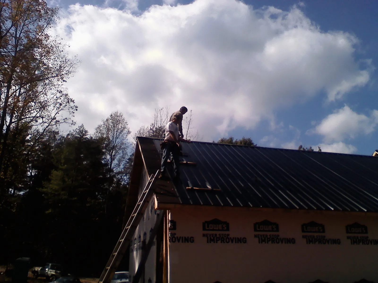 Roofer fastening dark metal panels high against a cloudy sky, from a Roof Inspection job in Peralta