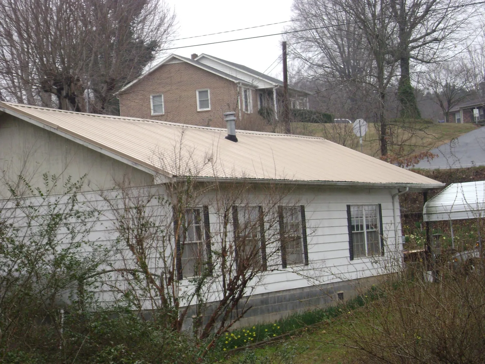 Tan metal roof on a white sided house set into a hillside — Commercial Roofing by Roofing Brothers in Peralta