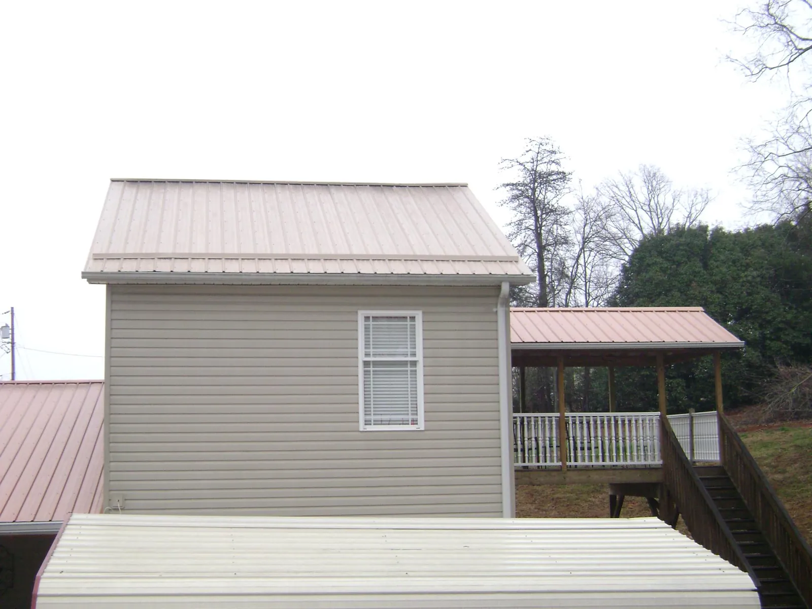 Tan metal roofs on a two story addition and attached porch, from a Roof Replacement job in Peralta